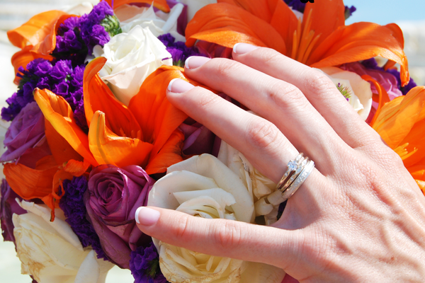 Close up of a women's hand earring an engagement ring and wedding ring over orange and purple floral wedding bouquet